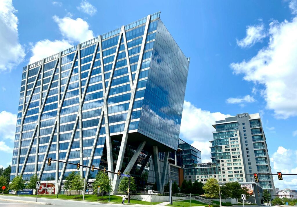 Tall modern office building with glass facade in an urban setting under a clear blue sky.