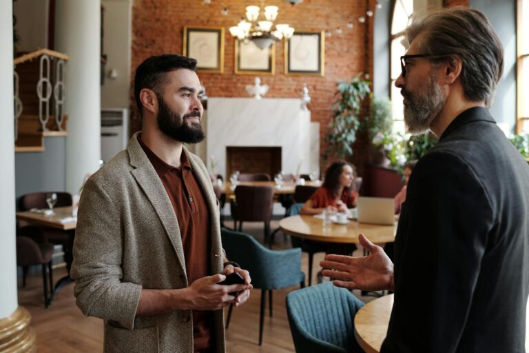 Two men engaged in a conversation inside a stylish cafe with brick walls and elegant decor.