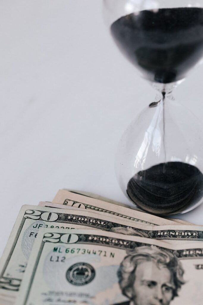 From above of hourglass with black sand near heap of paper money with image of president and official seal with numbers